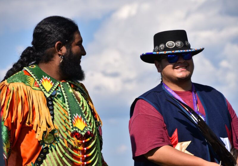 Two men in regalia smiling together at a community gathering