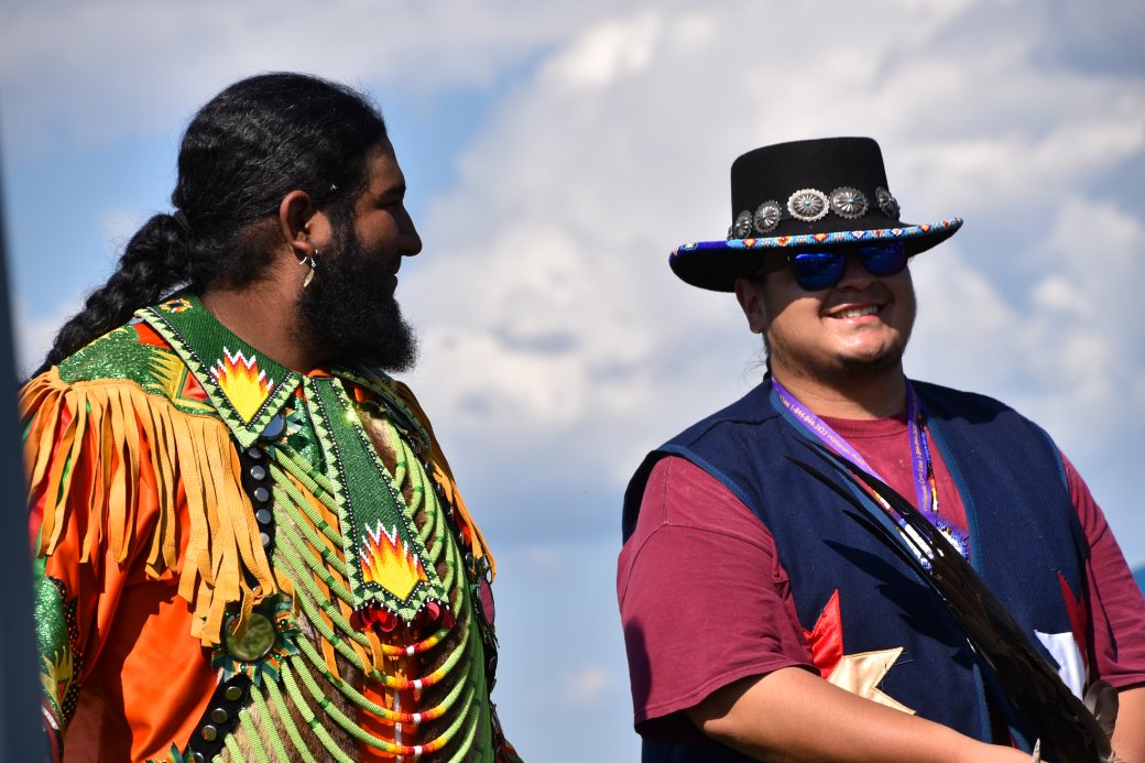 Two men in regalia smiling together at a community gathering