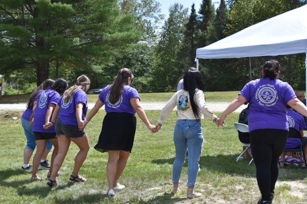 Young people in Wabanaki Public Health shirts holding hands in a circle dance
